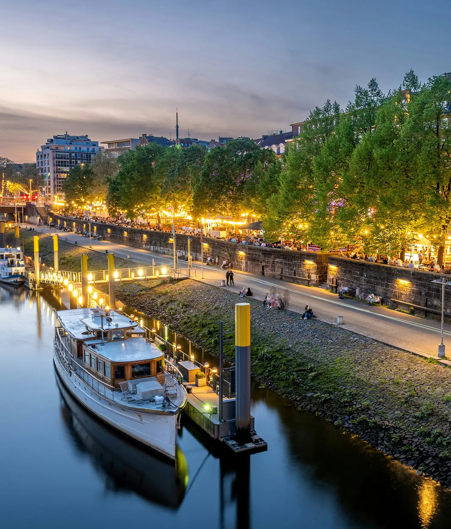 Die Bremer Schlachte an der Weser mit historischen Schiffen, Promenade und beleuchteten Restaurants am Abend.