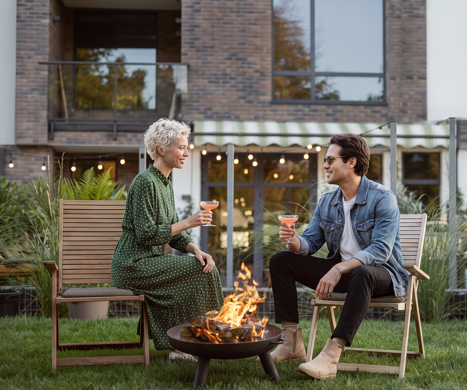 Zwei Personen sitzen vor einem modernen Wohnhaus an einer Feuerschale im Garten.